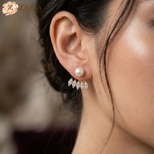 A cgold-toned Korean style 2-in-1 ear jacketlose-up photograph of a woman wearing a . The front is a classic white pearl stud, and a removable fan-shaped cluster of marquise-cut CZ stones sits behind the earlobe. The Zzilya Fashion logo is in the top left.