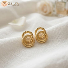 Pair of Zzilya Fashion gold interlocking stud earrings with twisted rope texture resting on a white fabric background.
