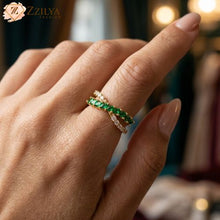 An adjustable golden anti-tarnish crossover ring by Zzilya Fashion, featuring one band of emerald green marquise stones and one band of clear round zircons, worn on a model's hand.