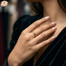 A delicate golden anti-tarnish ring with a leaf and vine cut-out pattern worn on a model's hand, styled with a dark green velvet outfit and neutral manicured nails by zzilya fashion jewellery