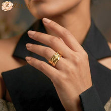 A wide, golden anti-tarnish statement ring with a textured, molten liquid-gold design worn on a model's hand against a sharp black blazer by zzilya fashion