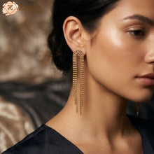 A close-up of a woman wearing long, cascading golden rhinestone dangle earrings by Zzilya Fashion, priced at 99 rupees.