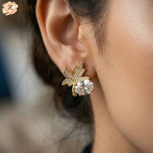 Pair of gold-plated maple leaf stud earrings featuring a large oval clear gemstone and small pavé-set crystals by Zzilya fashion