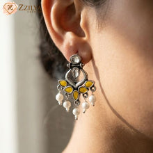 Close-up of a person wearing a decorative earring with yellow and white stones, branded 'Zzilya'.