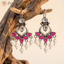 Ornate earrings with pink gemstones and pearl drops on a wooden branch background by zzilya fashion