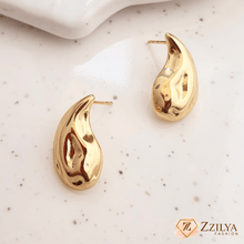 A pair of teardrop-shaped 18k gold plated earrings on a white surface, with the brand name 'Zzilya' visible.