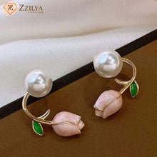 Pair of Zzilya Fashion gold-toned tulip and pearl stud earrings with pink enamel buds and green leaves on a dark brown display surface with the Zzilya logo in the corner.